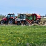 Agricultural Automation - a red tractor pulling a trailer of hay through a field