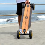 Electric Skateboard - person in black shorts and white shirt holding brown wooden skateboard on beach during daytime