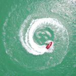 Personal Drone - aerial photography of red personal watercraft circling on water at daytime